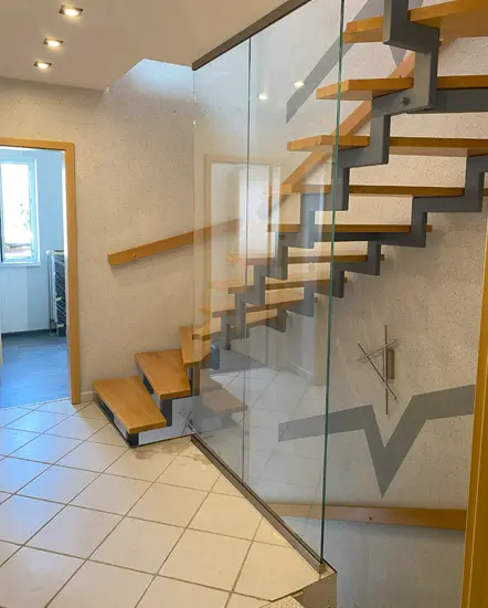 Moderne Treppe mit Glasgeländer und Holzstufen in einem lichtdurchfluteten Raum, ideal für stilvolle Innenarchitektur und Raumtrennung. AP Glas GmbH bietet maßgeschneiderte Lösungen für Glasbrüstungen und Glastreppengeländer.