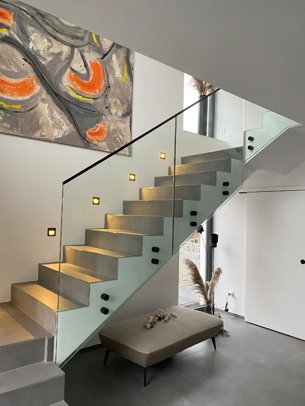 Modernes Glastreppengeländer in einem stilvollen Innenraum mit Betonstufen und Kunstwerk an der Wand, ideal für elegante Treppenlösungen von AP Glas GmbH.