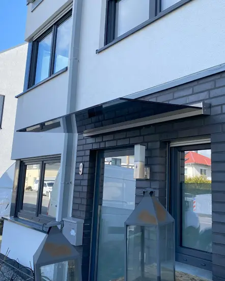 Glasvordach über einem Eingangsbereich, montiert von AP Glas GmbH, zeigt moderne Architektur und hochwertige Glasverarbeitung.