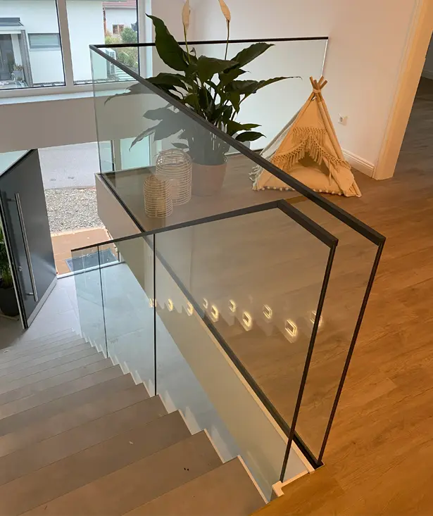 Moderne Glasbrüstung in einem Innenraum mit Holztreppe und Pflanzen, ideal für stilvolle Treppengeländer und Raumtrennungen.